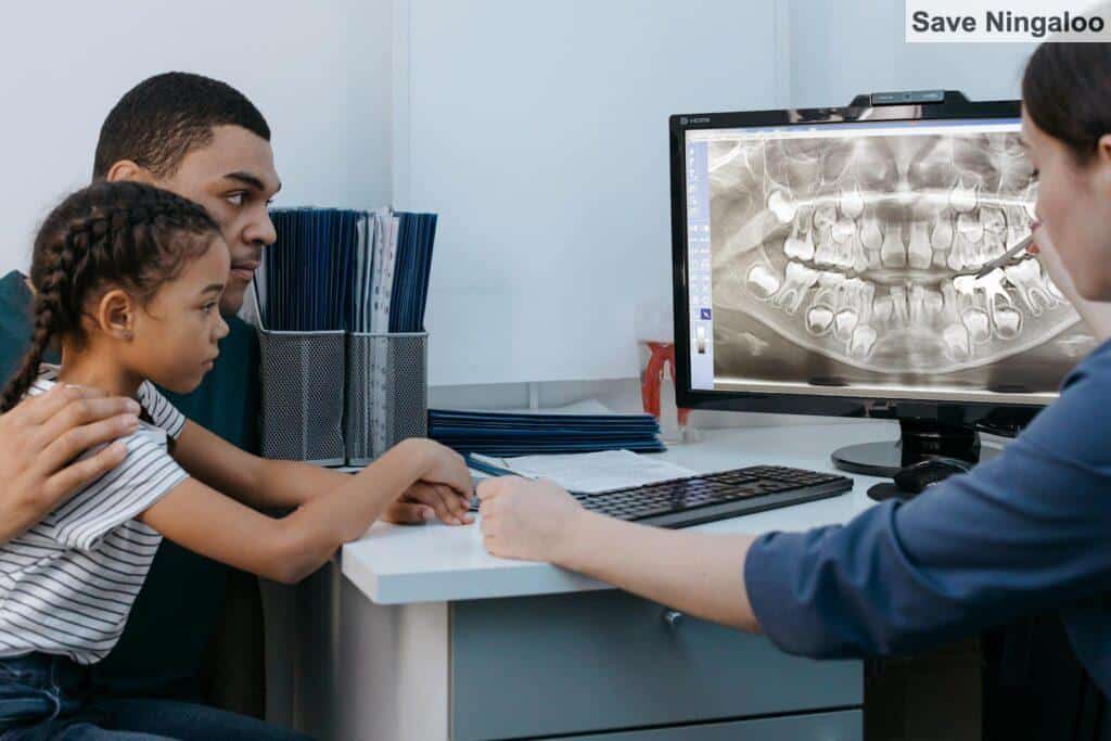 A father and daughter discuss dental care with a dentist reviewing an X-ray.